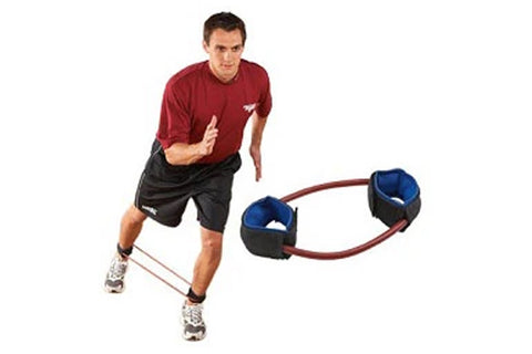 Man wearing burgundy shirt and black shorts demonstrating blue and black Theraband ankle cuff resistance trainer with red cor