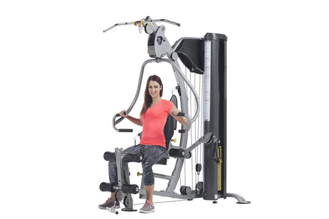 TuffStuff Classic home gym with silver frame, black seat, cable machine arms, and leg press attachment on white background