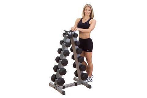 Woman in black sports bra and shorts standing next to dumbbell rack holding dumbbells, on white background