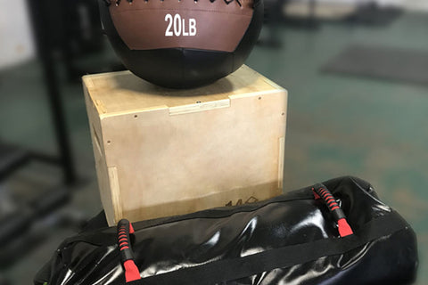 20lb medicine ball with brown leather upper and black rubber lower half on wooden box, next to black resistance training bag 