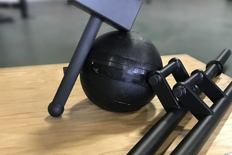 Black medicine ball with resistance bands and blue hammer on wooden surface, flat lay