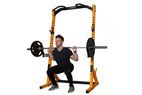 Yellow and black Powertec half rack with adjustable safety arms, shown with model performing barbell squat exercise