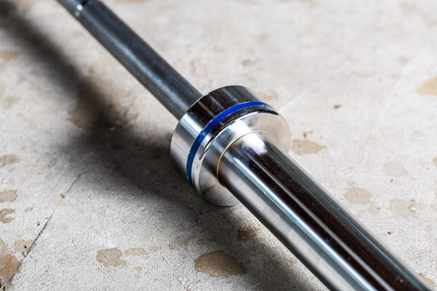 York Men's Elite Competition Olympic barbell with chrome finish, blue collar ring, and black shaft on concrete surface