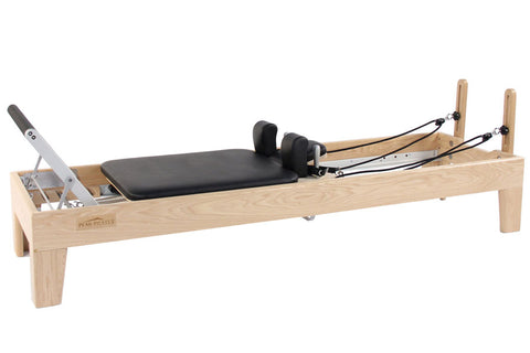 Light wood Pilates reformer with black padded seat, adjustable footbar, and resistance springs on white background