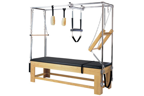 Pilates reformer with wood base, black padded bed, metal frame, and attached accessories including footbar, straps, and woode
