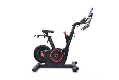 Black and red upright stationary exercise bike with tablet holder, handlebar grips, and weighted flywheel on white background
