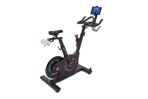 Black and red upright stationary exercise bike with tablet holder, handlebar grips, and weighted flywheel on white background