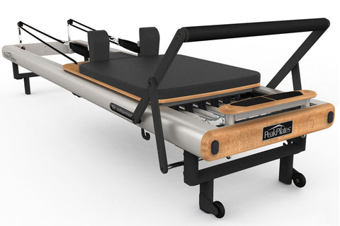Peak Pilates Fit Reformer with black upholstered platform, white barrel, natural wood footbar and handles, metal spring mecha