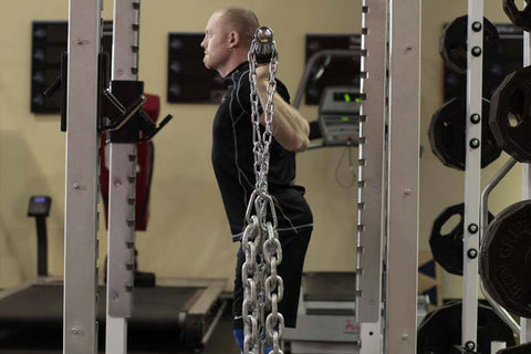 Man performing weighted exercise with heavy metal chain attached to squat rack in gym setting
