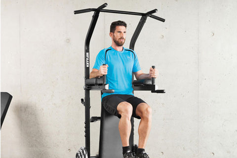 Black steel power tower with dual pull-up bars, dip handles, weight plate pegs, and padded seat, on white background