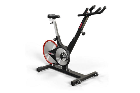 Black and red indoor stationary exercise bike with dual flywheels, black handlebars, gray seat post, and wide base on white b