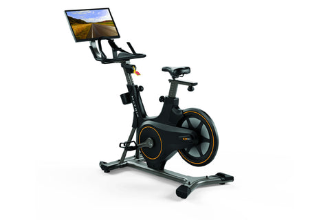 Black stationary exercise bike with orange accents, tablet console mounted on handlebar displaying road scenery, on white bac