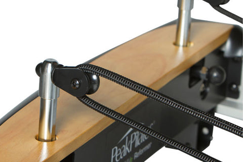 Pilates reformer with gray frame, black footplate, wooden accents, and adjustable carriage on white background
