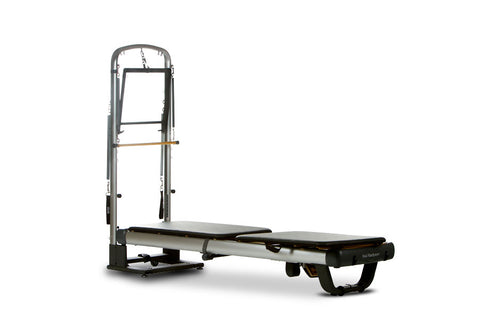 Peak Pilates reformer machine with gray metal frame, black padded carriage, and vertical tower on white background
