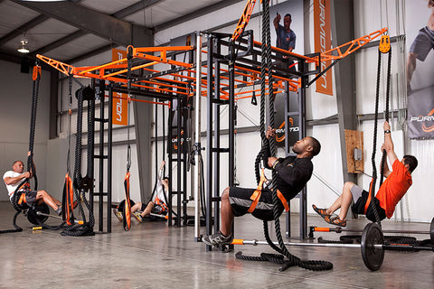 Orange and black functional training rig with multiple stations, rope attachments, and pull-up bars used by athletes in gym s