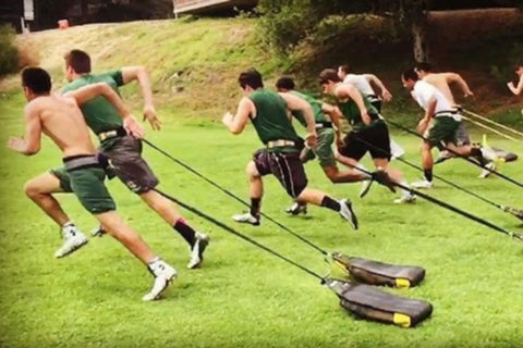 Multiple athletes performing sprint training with SKLZ SpeedSac Pro resistance sleds on grass field