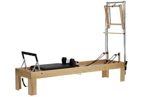 Wood and metal Pilates reformer with black padded carriage, springs, and tall tower frame on white background