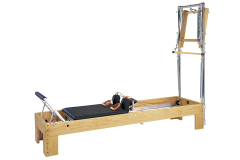Natural wood Pilates reformer with black mat, footbar, and metal tower frame on white background