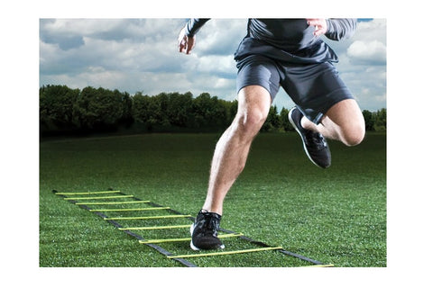 Male athlete in black shorts and shoes running through agility ladder on grass field outdoors