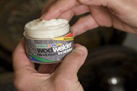 Warrior W.O.D. Welder white hand cream in jar held in palm, showing thick texture and colorful label with yellow and green st