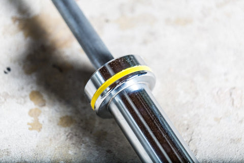 York Women's Elite Competition Olympic Bar with silver finish and yellow stripe band on concrete surface